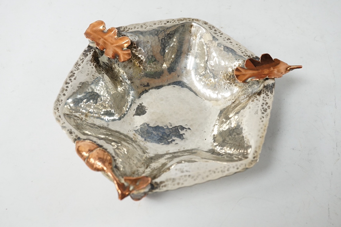 A 20th century Arts & Crafts planished white metal hexagonal dish, mounted with copper acorn and leaf surmounts, in the manner of Gorham & Co, diameter 12.8cm, gross weight 5.78oz. Condition - fair to good